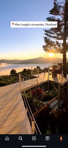 the sun is setting behind some trees and people are standing on a deck overlooking water