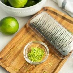 a cutting board with limes and a grater on it next to a bowl of guacamole