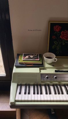 a green piano sitting next to a cup of coffee and a framed picture on the wall