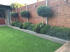 a wooden fence and some bushes in front of a building with grass on the ground