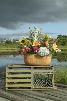 a basket filled with flowers sitting on top of a wooden crate next to a body of water