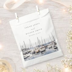 a white paper bag with a sailboat photo on it next to some flowers and wine glasses