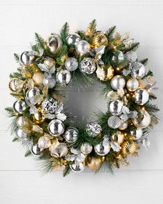 a christmas wreath with silver and gold ornaments hanging from the front of a white wall