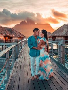 a man and woman standing on a pier at sunset