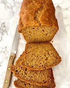 sliced loaf of banana bread sitting on top of a white counter next to a knife