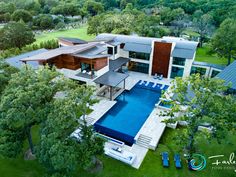 an aerial view of a house with a swimming pool in the foreground and trees surrounding it