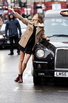 a woman leaning on the hood of a black car with her arms out in the air