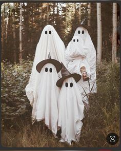 two people dressed up in ghost costumes standing in the woods with their heads covered by white cloths