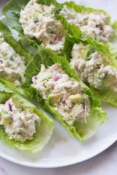 several lettuce leaves with chicken salad on them sitting on a white plate, ready to be eaten