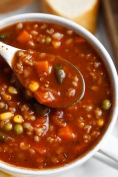 a spoon full of beans and carrots in a white bowl with bread on the side