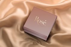 a pink box with the word rose on it laying on a satin fabric covered surface