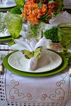 the table is set with green and white plates, napkins, and flowers in vases