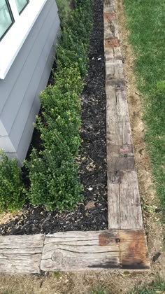 an old piece of wood is laying in the grass next to a white house and some bushes