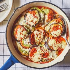 a skillet with some vegetables in it on a blue and white table cloth next to silverware