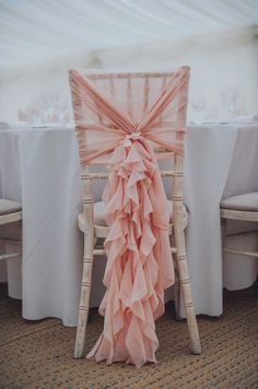 a chair covered in pink ruffles next to a table with white clothed tables