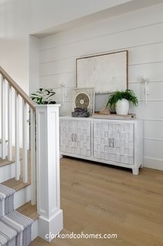 a white dresser sitting next to a wooden stair case in a room with wood floors