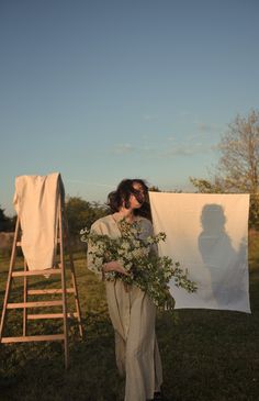 a woman holding flowers in front of a white sheet on a clothes line with a ladder behind her