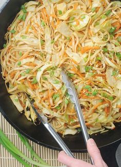 someone is cooking noodles in a skillet with green onions and carrots on the side