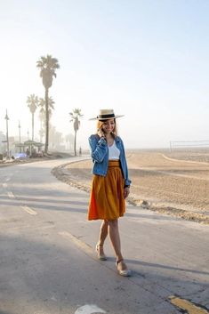 a woman standing on the side of a road talking on a cell phone while wearing a hat