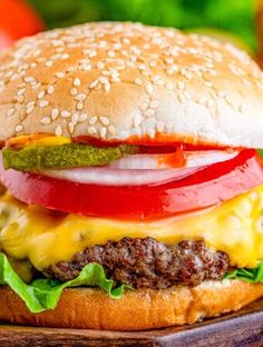 a cheeseburger with tomatoes, lettuce and pickles on a wooden cutting board