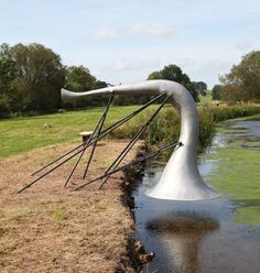 a sculpture sitting on top of a river next to a lush green field