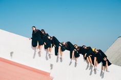 a group of women in graduation gowns sitting on the side of a building with their legs spread out