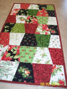 a quilted christmas table runner with poinsettis, holly and pine cones