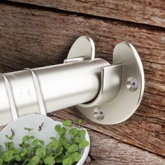 a white bowl filled with green plants next to a metal wall mounted hook on a wooden fence