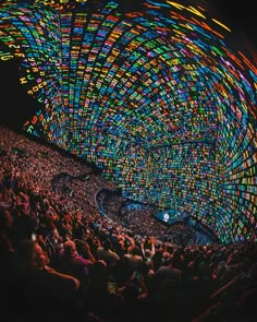 an audience at a concert with colorful lights on the ceiling and people sitting in the seats