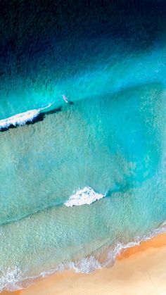 an aerial view of the ocean and beach with waves coming in from the water, as seen from above