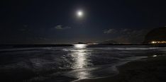 the moon is shining over the ocean at night