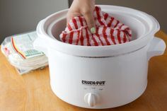 a person is cleaning the inside of an electric crock pot with a red and white striped cloth