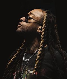 a man with long dreadlocks and sunglasses looking up into the sky in front of a black background