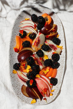 a white plate topped with sliced fruit and blackberries on top of a bed of linen