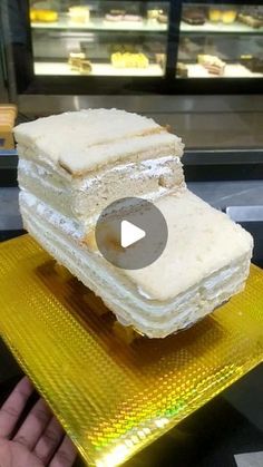 a person is holding up a cake with white frosting on it in front of a display case