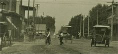 an old black and white photo of people walking down a dirt road with horse drawn carriages