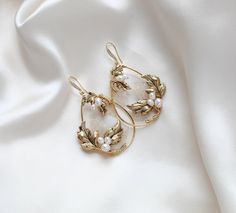 These handcrafted antique gold wedding earrings showcase a boho-inspired floral design, featuring delicate leaves and freshwater pearls. Expertly made to order, these hoop earrings add a touch of elegance and uniqueness to any bridal look. - Handcrafted in my PA studio - Genuine Austrian golden shadow crystal rock fabric leaves - Freshwater pearls - Antique gold leaves  - Available in rose gold, yellow gold or rhodium (silver) - Earrings measure 2.5 inches x 1-5/8 inch - Handcrafted in the US. - Nickel free and hypoallergenic - PLEASE ALLOW APPROX 10 BUSINESS DAYS FOR COMPLETION BEFORE SHIPPING. This is an original design by © Treasures by Agnes Browse our earrings: https://www.etsy.com/shop/treasures570?ref=seller-platform-mcnav&section_id=6861728 Browse our backdrop necklaces: https://ww Vintage Gold Flower Earrings For Wedding, Brass Filigree Hoop Earrings For Wedding, Handmade Delicate Yellow Gold Pearl Earrings, Delicate Handmade Gold Pearl Earrings, Delicate Handmade Yellow Gold Pearl Earrings, Elegant Gold Flower Earrings For Wedding, Wedding Pearl Drop Brass Earrings, Wedding Pearl Drop Earrings In Brass, Dainty Yellow Gold Pearl Earrings For Wedding