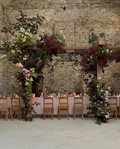 a table set up with flowers and candles for an outdoor wedding reception in front of a stone wall