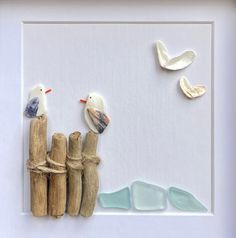 three seagulls sitting on top of driftwood in front of a white frame