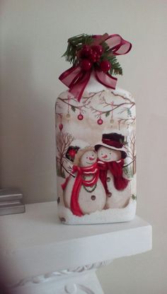 a glass jar with two snowmen in it and a red bow on the top