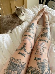 a cat laying on top of a bed next to a person with tattoos on their legs