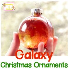 a person holding up a christmas ornament in front of a window with the words galaxy on it