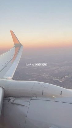 the wing of an airplane as it flies above the cityscape at sunset or dawn