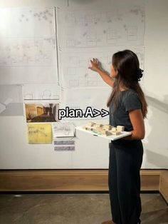 a woman holding a tray with cookies on it in front of a white board that has drawings on it