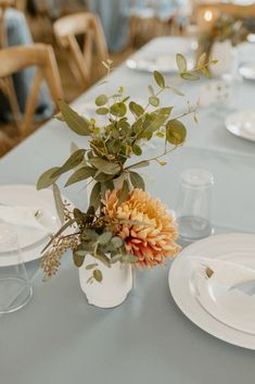 an arrangement of flowers in a vase on a table with plates and glasses around it