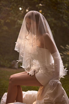 a woman in a white wedding dress and veil sitting on a bench with her legs crossed