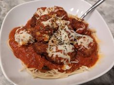 a white bowl filled with meatballs and sauce on top of pasta covered in parmesan cheese