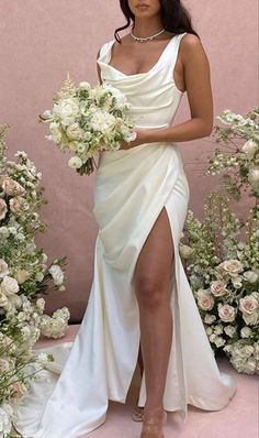 a woman in a white dress holding a bouquet and posing for the camera with her legs crossed