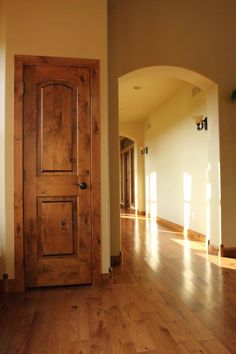 an empty hallway with a wooden door and hard wood flooring in the foreground