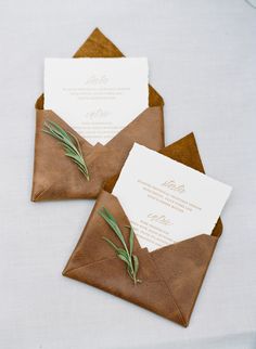 two brown envelopes with white paper and greenery are on top of each other